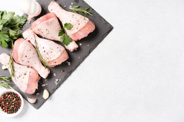 Raw chicken drumsticks with seasonings on black slate plate over white concrete background with copy space. Chicken legs ready to cook. Dietary meat, healthy eating concept