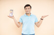 Portrait of happy Indian man holding glass jar full of rupee notes in one hand and other hand is empty to put advertisement isolated on beige studio background. Money saving and investing concept.