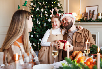 Sticker - Cute happy little girl getting xmas gift present from loving parents during Christmas dinner