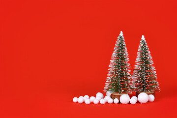 Wall Mural - Miniature Christmas trees and snowballs on red background with copy space