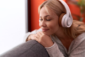 Wall Mural - Young blonde woman listening to music sitting on sofa at home