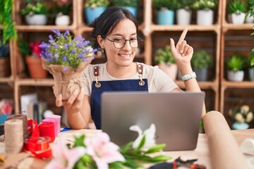 Sticker - Young hispanic woman working at florist shop doing video call smiling amazed and surprised and pointing up with fingers and raised arms.