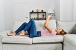 © Krakenimages.com - Young woman using smartphone lying on sofa at home