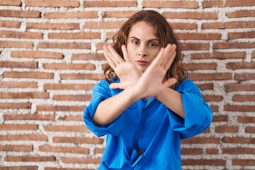 Poster - Beautiful brunette woman standing over bricks wall rejection expression crossing arms and palms doing negative sign, angry face