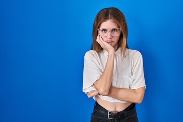 Wall Mural - Beautiful woman standing over blue background thinking looking tired and bored with depression problems with crossed arms.