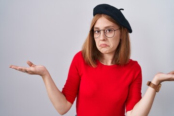 Poster - Young redhead woman standing wearing glasses and beret clueless and confused expression with arms and hands raised. doubt concept.