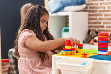 Wall Mural - Plus size hispanic girl playing with construction blocks sitting on table at kindergarten