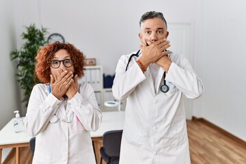 Wall Mural - Two middle age doctors at medical clinic shocked covering mouth with hands for mistake. secret concept.