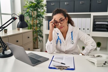 Wall Mural - Young hispanic woman wearing doctor uniform and stethoscope worried and stressed about a problem with hand on forehead, nervous and anxious for crisis