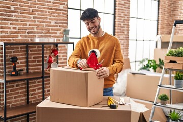 Wall Mural - Young hispanic man smiling confident packing cardboard box at new home