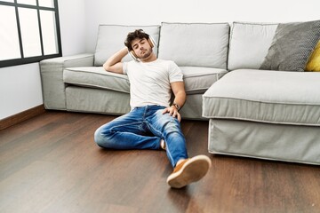 Sticker - Young hispanic man listening to music sitting on the floor at home