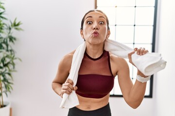 Wall Mural - Young hispanic woman wearing sportswear and towel at sport center looking at the camera blowing a kiss being lovely and sexy. love expression.