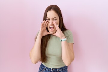 Poster - Beautiful brunette woman standing over pink background shouting angry out loud with hands over mouth