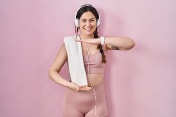 Sticker - Young brunette woman wearing sportswear and headphones gesturing with hands showing big and large size sign, measure symbol. smiling looking at the camera. measuring concept.