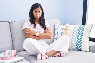 Sticker - Young hispanic woman sitting on the sofa at home skeptic and nervous, disapproving expression on face with crossed arms. negative person.