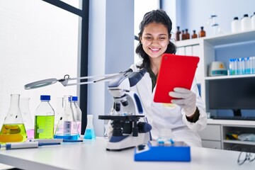 Sticker - Young latin woman scientist using microscope and touchpad at laboratory