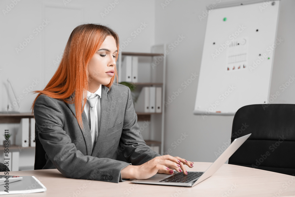 Beautiful transgender secretary working with laptop at table in office