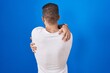 © Krakenimages.com - Young caucasian man standing over blue background hugging oneself happy and positive from backwards. self love and self care
