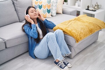 Sticker - Young chinese woman listening to music sitting on floor at home