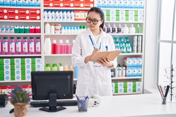 Sticker - Young chinese woman pharmacist writing on notebook using computer at pharmacy