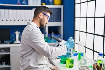 Sticker - Young hispanic man wearing scientist uniform measuring liquid at laboratory