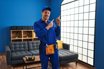 Canvas Print - Young hispanic working at home renovation smiling and looking at the camera pointing with two hands and fingers to the side.