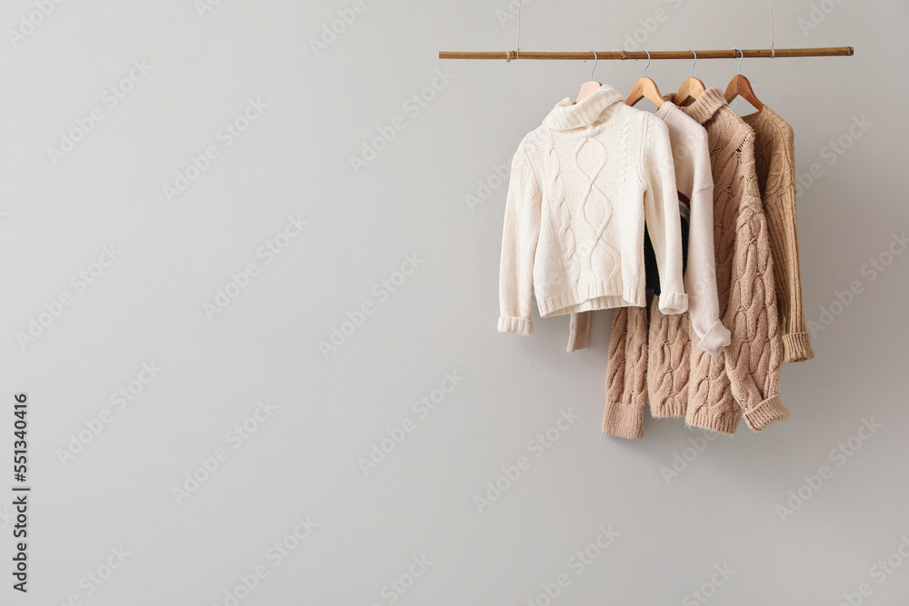 Rack with knitted sweaters hanging on light wall