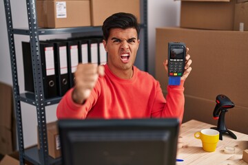 Poster - Hispanic man working at small business ecommerce holding dataphone annoyed and frustrated shouting with anger, yelling crazy with anger and hand raised