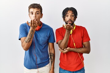 Wall Mural - Young hispanic brothers standing over isolated background wearing headphones looking at the camera blowing a kiss with hand on air being lovely and sexy. love expression.