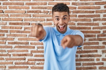 Canvas Print - Brazilian young man standing over brick wall pointing to you and the camera with fingers, smiling positive and cheerful