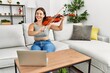 Young beautiful hispanic woman having online violin class sitting on sofa at home