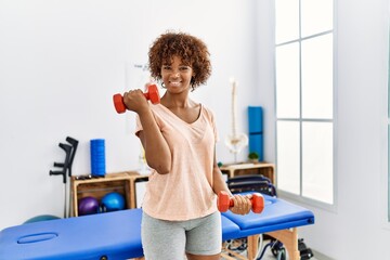 Poster - Young african american woman doing rehab using dumbbells at clinic