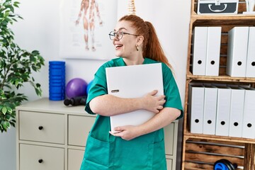 Wall Mural - Young redhead woman wearing phsiologist uniform holding binder at clinic