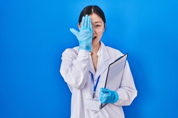 Poster - Chinese young woman working at scientist laboratory covering one eye with hand, confident smile on face and surprise emotion.