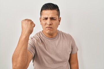 Canvas Print - Hispanic young man standing over white background angry and mad raising fist frustrated and furious while shouting with anger. rage and aggressive concept.