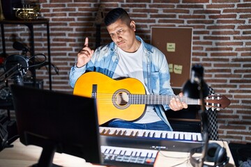 Sticker - Hispanic young man playing classic guitar at music studio pointing up looking sad and upset, indicating direction with fingers, unhappy and depressed.