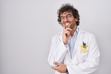 Poster - Hispanic young man wearing doctor uniform looking confident at the camera smiling with crossed arms and hand raised on chin. thinking positive.