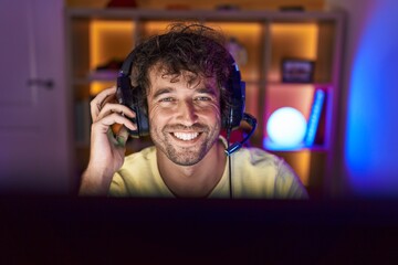 Young hispanic man streamer smiling confident sitting on table at gaming room