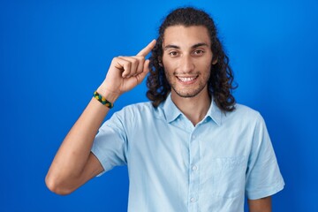 Poster - Young hispanic man standing over blue background smiling pointing to head with one finger, great idea or thought, good memory