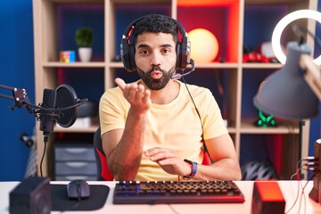 Wall Mural - Hispanic man with beard playing video games with headphones looking at the camera blowing a kiss with hand on air being lovely and sexy. love expression.