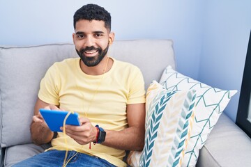 Sticker - Young arab man using touchpad sitting on sofa at home