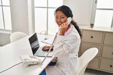 Wall Mural - Young chinese woman wearing doctor uniform talking on the telephone at clinic