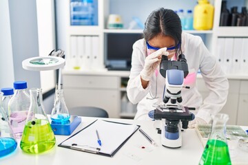 Wall Mural - Young chinese woman wearing scientist uniform using microscope at laboratory