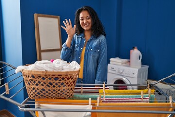 Poster - Young asian woman hanging clothes at clothesline showing and pointing up with fingers number five while smiling confident and happy.