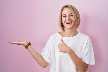 Canvas Print - Young caucasian woman standing over pink background showing palm hand and doing ok gesture with thumbs up, smiling happy and cheerful