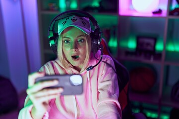 Poster - Young caucasian woman playing video games with smartphone pointing thumb up to the side smiling happy with open mouth