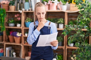 Poster - Young blonde woman florist reading document with doubt expression at florist