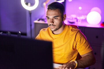 Young hispanic man streamer playing video game using computer at gaming room