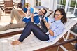 © Krakenimages.com - Middle age hispanic couple using smartphone and touchpad lying on hammock with dog at terrace