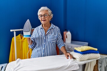 Wall Mural - Senior grey-haired woman smiling confident ironing clothes at laundry room